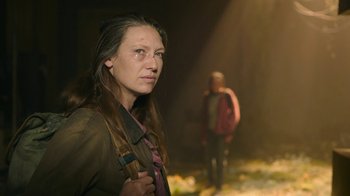 Movie still from “The Last of Us” (2023), created by Neil Druckmann – A woman holding a knife in her hand while standing next to a man; Medium shot, Over the shoulder angle