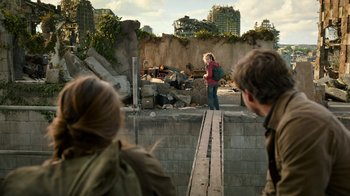 Movie still from “The Last of Us” (2023), created by Neil Druckmann – A girl standing on top of a wooden bridge near rocks; Wide shot, Over the shoulder angle