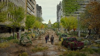 Movie still from “The Last of Us” (2023), created by Neil Druckmann – Two people walking down a dirt path in a city; Extreme Wide shot, High angle