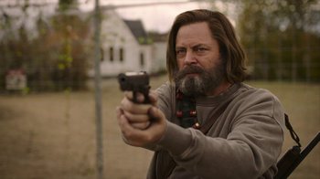 Movie still from “The Last of Us” (2023), created by Neil Druckmann – A man holding a gun while standing in front of a building; Medium shot, Low angle