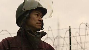 Movie still from “The Last of Us” (2023), created by Neil Druckmann – A man wearing a motorcycle helmet while standing in front of barbed wire; Close Up shot, Low angle