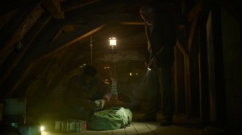 Movie still from “The Last of Us” (2023), created by Neil Druckmann – Two men in a room with a flashlight and a bag; Wide shot, Low angle