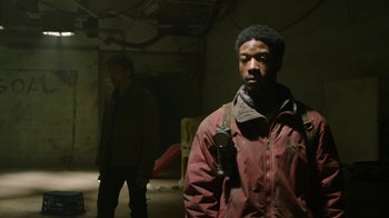 Movie still from “The Last of Us” (2023), created by Neil Druckmann – A man in a red jacket standing next to another man in a brown jacket; Medium shot, Over the shoulder angle