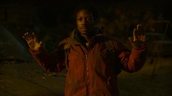 Movie still from “The Last of Us” (2023), created by Neil Druckmann – A man in a red jacket with his arms raised; Medium shot, Low angle