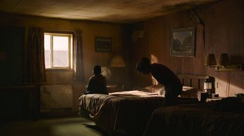 Movie still from “The Last of Us” (2023), created by Neil Druckmann – Two people sitting on a bed in a room; Wide shot, Low angle
