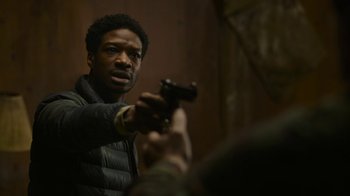 Movie still from “The Last of Us” (2023), created by Neil Druckmann – A man holding a gun in his hand and looking at the camera; Close Up shot, Over the shoulder angle