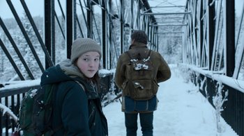 Movie still from “The Last of Us” (2023), created by Neil Druckmann – Two people walking across a bridge in the snow; Medium shot, Over the shoulder angle