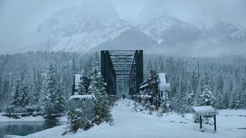 Movie still from “The Last of Us” (2023), created by Neil Druckmann – A bridge over a river in the middle of a snowy forest; Extreme Wide shot, Low angle