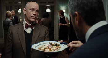 Movie still from “Burn After Reading” (2008), directed by Joel Coen – A man holding a plate with food on top of it; Medium shot, Over the shoulder angle