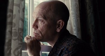 Movie still from “Burn After Reading” (2008), directed by Joel Coen – A bald man sitting in front of a window with his hand under his chin; Close Up shot, Low angle