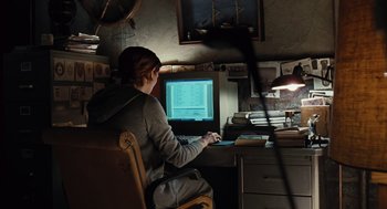 Movie still from “Burn After Reading” (2008), directed by Joel Coen – A woman sitting in front of a computer on top of a desk; Medium shot, High angle