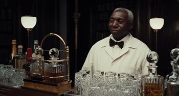 Movie still from “Burn After Reading” (2008), directed by Joel Coen – An older man standing next to a table full of glasses; Medium shot, Over the shoulder angle