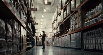 Movie still from “Burn After Reading” (2008), directed by Joel Coen – A man is standing in a warehouse looking at boxes; Wide shot, High angle