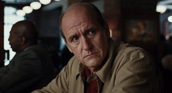 Movie still from “Burn After Reading” (2008), directed by Joel Coen – An older man wearing a tan shirt and a red tie; Close Up shot, Over the shoulder angle