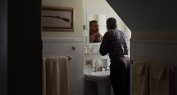 Movie still from “Burn After Reading” (2008), directed by Joel Coen – An older man looking in the bathroom mirror while a younger man brushes his teeth in front of the mirror; Medium shot, Over the shoulder angle