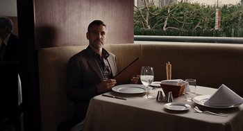 Movie still from “Burn After Reading” (2008), directed by Joel Coen – A man sitting at a table in front of a plate of food; Medium shot, Over the shoulder angle