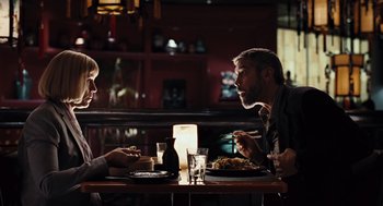 Movie still from “Burn After Reading” (2008), directed by Joel Coen – Two people sitting at a dinner table with food; Medium shot, Over the shoulder angle