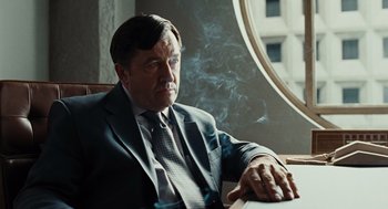 Movie still from “Burn After Reading” (2008), directed by Joel Coen – A man in a suit and tie sitting at a table; Close Up shot, Low angle