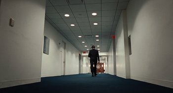 Movie still from “Burn After Reading” (2008), directed by Joel Coen – A man in a suit and tie walking down a hall way; Wide shot, High angle