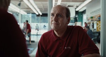 Movie still from “Burn After Reading” (2008), directed by Joel Coen – An older man in a red shirt is sitting in a room; Close Up shot, Over the shoulder angle