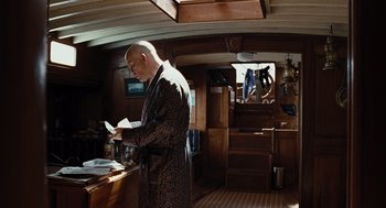 Movie still from “Burn After Reading” (2008), directed by Joel Coen – A man in a robe standing in front of a counter; Medium shot, Low angle