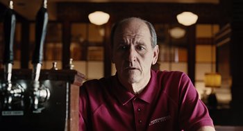 Movie still from “Burn After Reading” (2008), directed by Joel Coen – An older man in a red shirt is sitting at a table; Close Up shot, Low angle