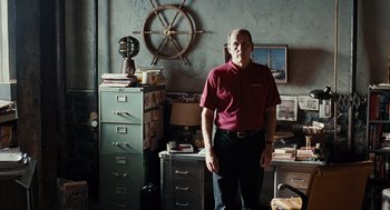 Movie still from “Burn After Reading” (2008), directed by Joel Coen – A man standing in front of a desk in a cluttered room; Medium shot, Low angle