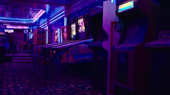 Movie still from “The Last of Us” (2023), created by Neil Druckmann – A row of arcade machines in a room lit up with neon lights; Extreme Wide shot, High angle