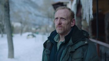 Movie still from “The Last of Us” (2023), created by Neil Druckmann – A person wearing a jacket near a building; Close Up shot, Low angle