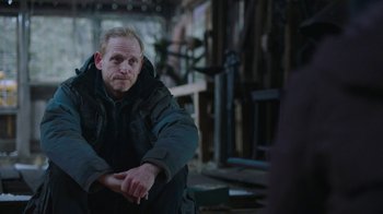 Movie still from “The Last of Us” (2023), created by Neil Druckmann – A man sitting on a chair in a room; Medium shot, Over the shoulder angle