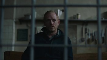 Movie still from “The Last of Us” (2023), created by Neil Druckmann – A man sitting in front of a window looking at the camera; Medium shot, Over the shoulder angle