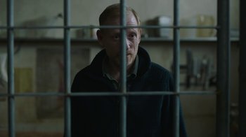 Movie still from “The Last of Us” (2023), created by Neil Druckmann – A man standing behind bars in a jail cell; Medium shot, Over the shoulder angle