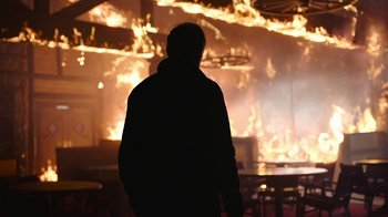 Movie still from “The Last of Us” (2023), created by Neil Druckmann – A man standing in front of a burning building; Wide shot, Over the shoulder angle