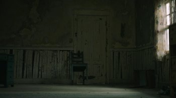 Movie still from “The Last of Us” (2023), created by Neil Druckmann – An empty chair in front of an open door; Wide shot, High angle