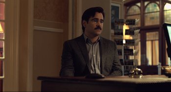 Movie still from “The Lobster” (2015), directed by Yorgos Lanthimos – A man sitting at a table in a room; Medium shot, Over the shoulder angle