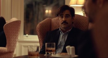 Movie still from “The Lobster” (2015), directed by Yorgos Lanthimos – A man sitting at a table with a drink in front of him; Close Up shot, Over the shoulder angle