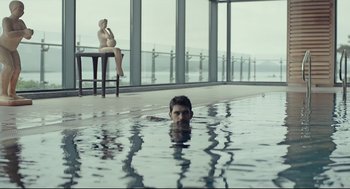 Movie still from “The Lobster” (2015), directed by Yorgos Lanthimos – A man swimming in a pool with a woman sitting on a bench in front of him; Wide shot, Over the shoulder angle