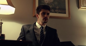 Movie still from “The Lobster” (2015), directed by Yorgos Lanthimos – A man wearing a suit and tie in front of a painting; Medium shot, Low angle
