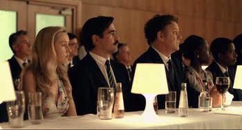 Movie still from “The Lobster” (2015), directed by Yorgos Lanthimos – A group of people sitting at a table with a lamp; Medium shot, Over the shoulder angle