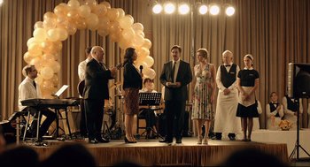 Movie still from “The Lobster” (2015), directed by Yorgos Lanthimos – A group of people standing on a stage with a microphone; Wide shot, Over the shoulder angle