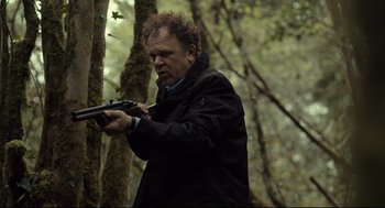 Movie still from “The Lobster” (2015), directed by Yorgos Lanthimos – A man holding a gun while standing next to a tree; Medium shot, Low angle