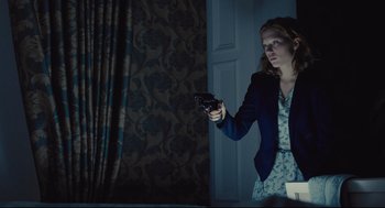 Movie still from “The Lobster” (2015), directed by Yorgos Lanthimos – A woman holding a gun while standing next to a door; Medium shot, Low angle