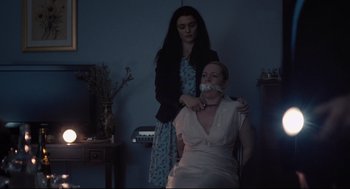 Movie still from “The Lobster” (2015), directed by Yorgos Lanthimos – A woman standing next to another woman with a gag in her mouth; Medium shot, Over the shoulder angle