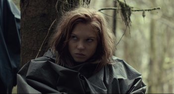 Movie still from “The Lobster” (2015), directed by Yorgos Lanthimos – A woman in a raincoat standing next to a tree in the woods; Medium shot, Low angle