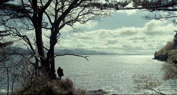Movie still from “The Lobster” (2015), directed by Yorgos Lanthimos – A person standing next to a tree near the water; Extreme Wide shot, Low angle