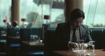 Movie still from “The Lobster” (2015), directed by Yorgos Lanthimos – A man sitting at a table in front of a glass of water; Medium shot, Over the shoulder angle