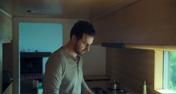 Movie still from “The Lodge” (2019), directed by Severin Fiala – A man standing in a kitchen preparing a meal; Medium shot, Low angle