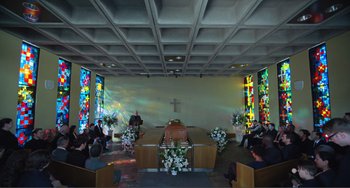 Movie still from “The Lodge” (2019), directed by Severin Fiala – People sit in a church with a casket in the foreground; Wide shot, High angle