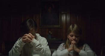 Movie still from “The Lodge” (2019), directed by Severin Fiala – Two young girls sitting at a table with their hands in their mouths; Medium shot, Low angle
