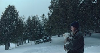 Movie still from “The Lodge” (2019), directed by Severin Fiala – A woman holding a cat in her arms in the snow; Wide shot, Over the shoulder angle
